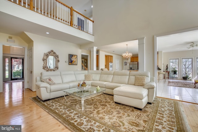 living area with a towering ceiling, light wood finished floors, ceiling fan, decorative columns, and a chandelier