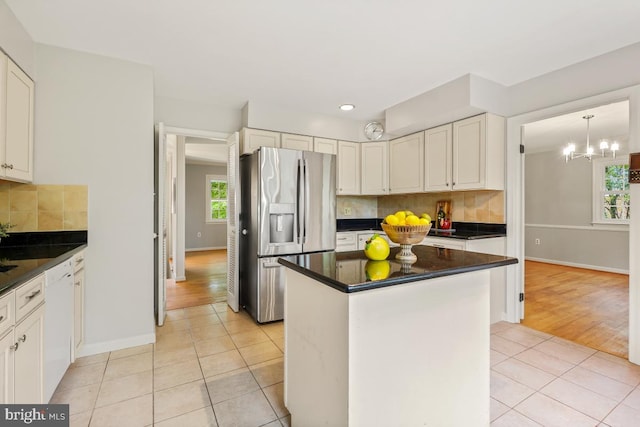 kitchen with stainless steel refrigerator with ice dispenser, dark countertops, light tile patterned flooring, white dishwasher, and baseboards