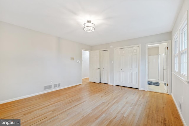 unfurnished bedroom featuring multiple closets, light wood finished floors, baseboards, and ensuite bathroom