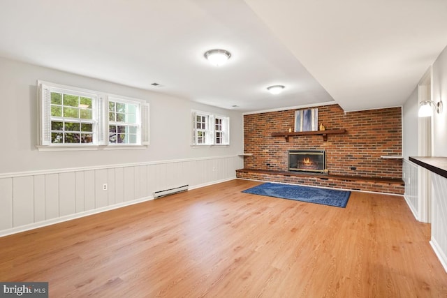 unfurnished living room with a baseboard heating unit, light wood-type flooring, a brick fireplace, and a wainscoted wall