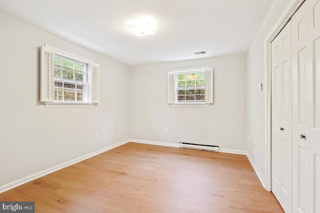 unfurnished bedroom with baseboard heating, a closet, light wood-style flooring, and baseboards