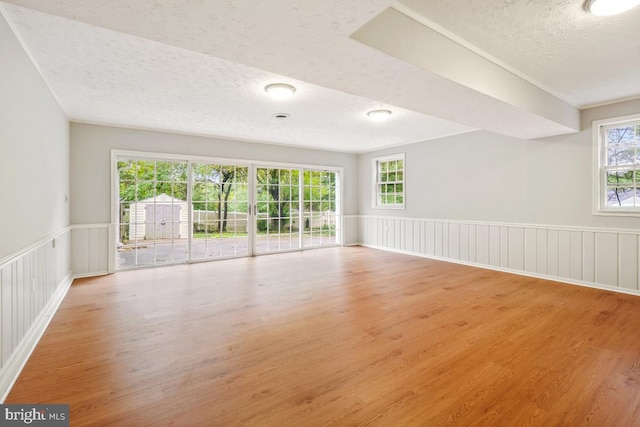 spare room featuring a textured ceiling, wainscoting, wood finished floors, and a decorative wall