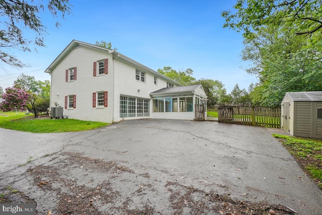 rear view of house with a sunroom, central AC unit, a shed, an outbuilding, and stucco siding