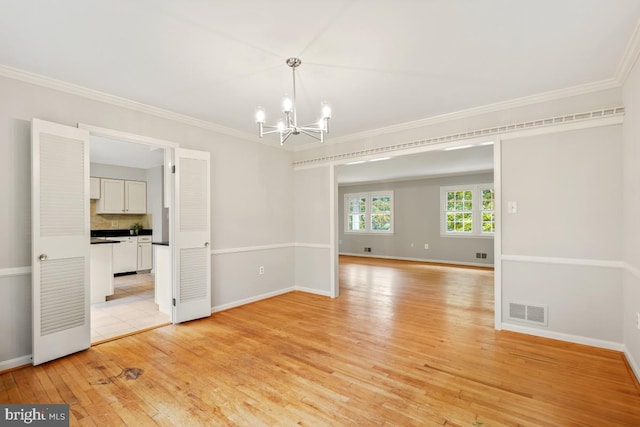 spare room featuring a chandelier, light wood-style floors, crown molding, and baseboards