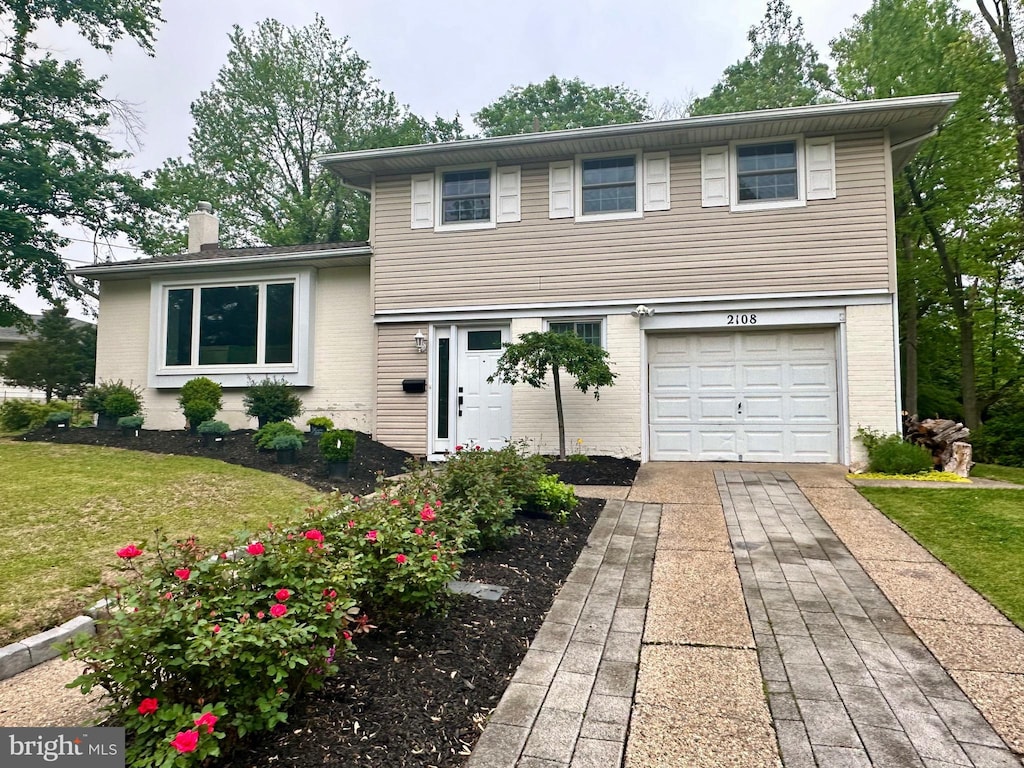 tri-level home with an attached garage, a chimney, concrete driveway, a front lawn, and brick siding
