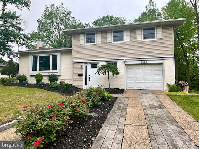 tri-level home with an attached garage, a chimney, concrete driveway, a front lawn, and brick siding