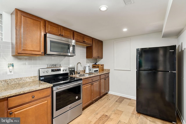 kitchen featuring appliances with stainless steel finishes, a sink, light wood-style flooring, brown cabinets, and recessed lighting