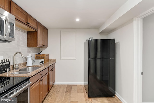 kitchen with stainless steel appliances, light wood-style floors, light stone countertops, brown cabinets, and backsplash