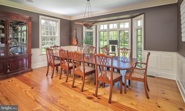 dining area featuring wainscoting, a decorative wall, light wood-type flooring, and ornamental molding