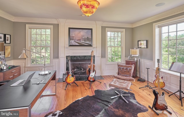 living area featuring plenty of natural light, wood-type flooring, a premium fireplace, crown molding, and wainscoting