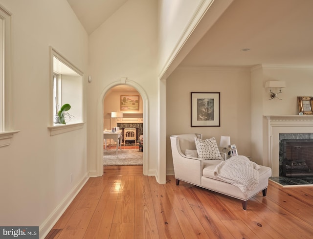 living area with a fireplace, arched walkways, light wood-style floors, baseboards, and vaulted ceiling