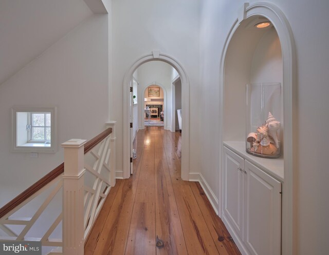 hall with arched walkways, light wood-style flooring, an upstairs landing, and high vaulted ceiling