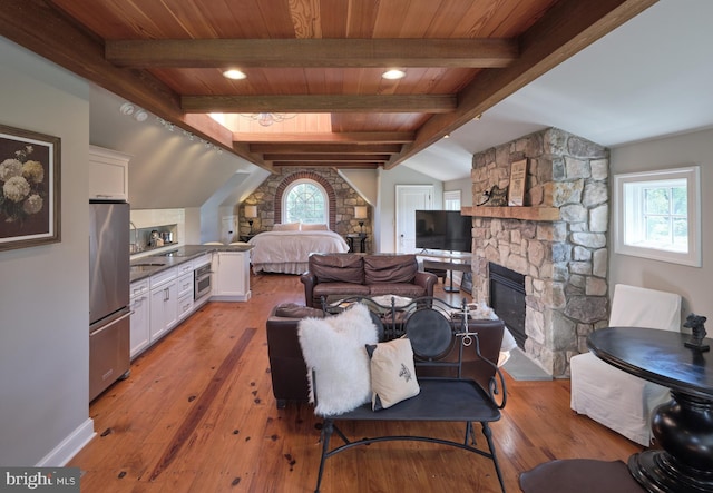 living area with a stone fireplace, light wood finished floors, baseboards, and wood ceiling