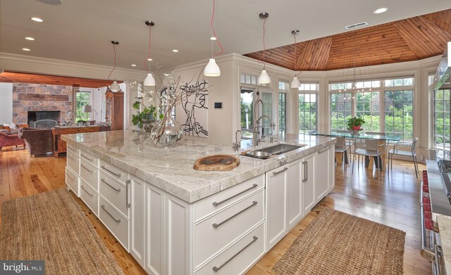 kitchen with a sink, lofted ceiling, a spacious island, light wood finished floors, and white cabinetry