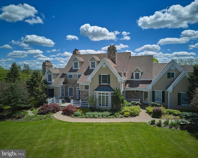 shingle-style home with a chimney, a front lawn, and stone siding