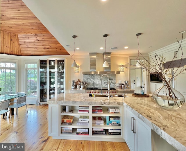 kitchen featuring wall chimney exhaust hood, open shelves, backsplash, light stone counters, and recessed lighting