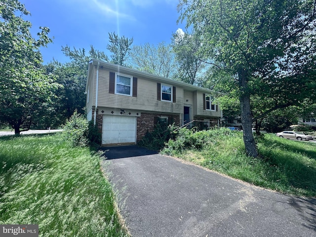 raised ranch with an attached garage, brick siding, and driveway