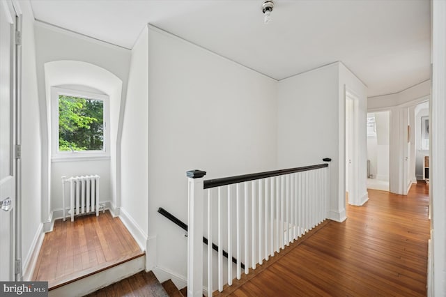 corridor with radiator heating unit, an upstairs landing, wood-type flooring, ornamental molding, and baseboards
