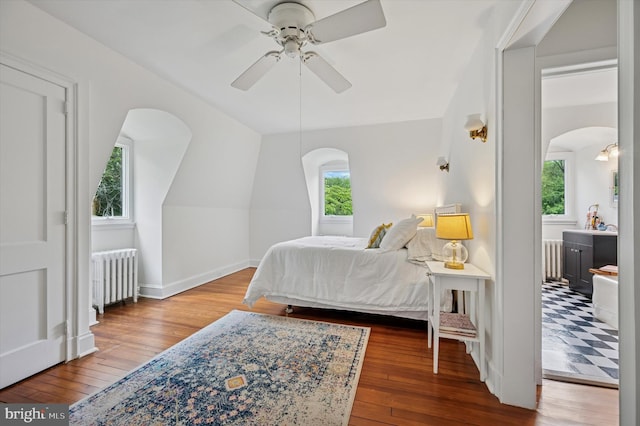 bedroom featuring radiator, arched walkways, hardwood / wood-style flooring, baseboards, and lofted ceiling