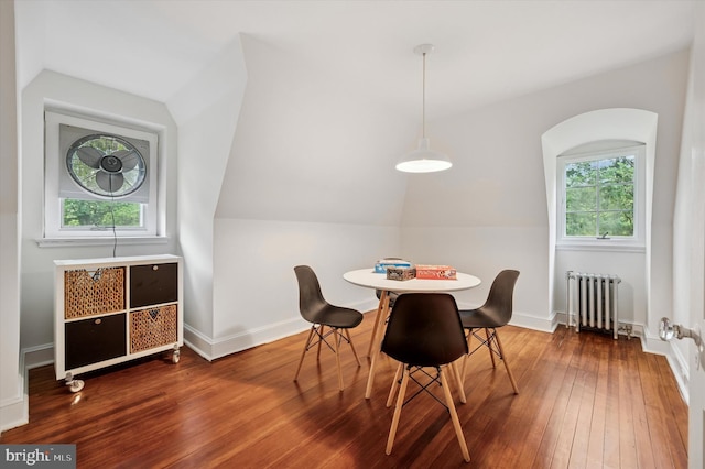 dining area featuring radiator heating unit, vaulted ceiling, hardwood / wood-style flooring, and baseboards