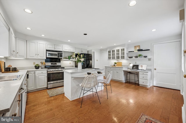 kitchen with appliances with stainless steel finishes, open shelves, white cabinetry, a sink, and light wood-type flooring