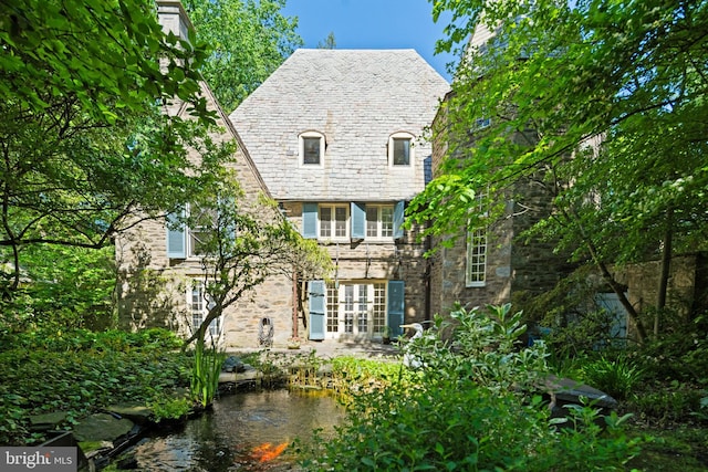 rear view of property with a high end roof and stone siding