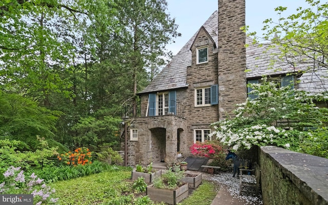 rear view of house with a high end roof, stone siding, and a garden