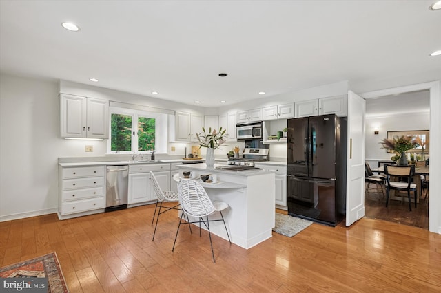 kitchen with stainless steel appliances, a sink, light countertops, white cabinets, and light wood finished floors