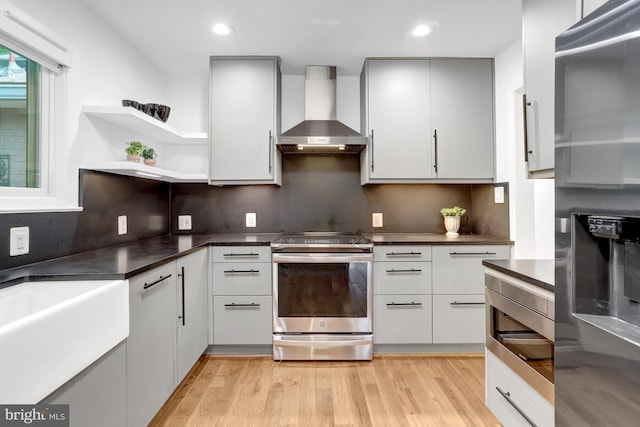 5018 36th St N, Arlington, VA 22207 - kitchen with wall chimney exhaust hood, appliances with stainless steel finishes, dark countertops, light wood-style floors, and recessed lighting