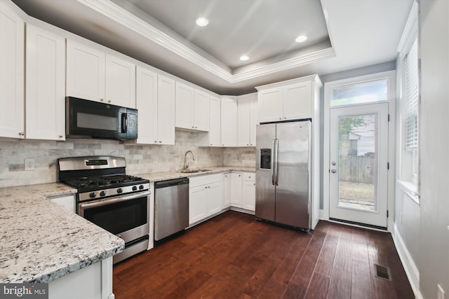 kitchen with appliances with stainless steel finishes, a sink, dark wood finished floors, ornamental molding, and white cabinets