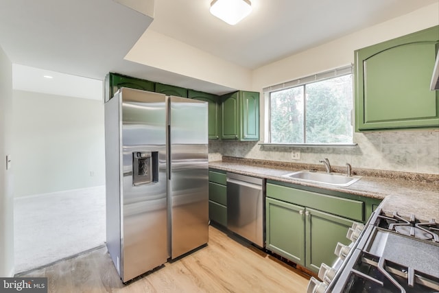 kitchen featuring green cabinetry, stainless steel appliances, a sink, light wood finished floors, and decorative backsplash