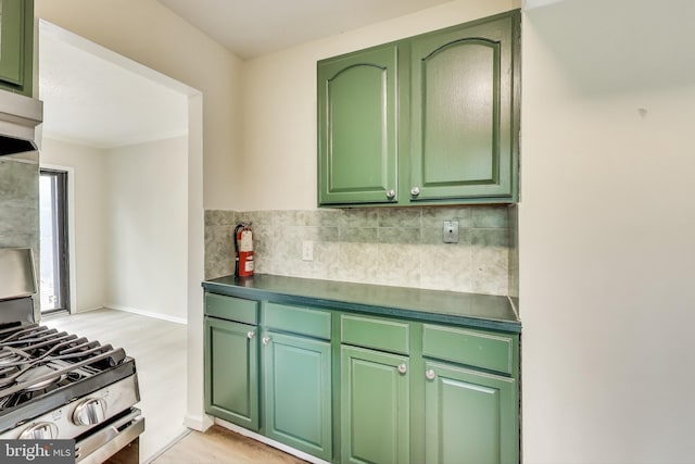 kitchen with stainless steel gas range, green cabinets, decorative backsplash, dark countertops, and light wood-style floors
