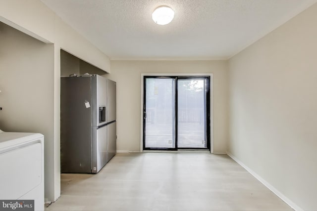 unfurnished dining area featuring washer / clothes dryer, a textured ceiling, light wood-style flooring, and baseboards