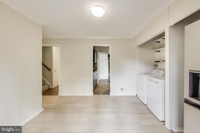 washroom with separate washer and dryer, light wood-style flooring, a textured ceiling, and baseboards
