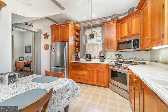 kitchen with pendant lighting, brown cabinetry, light countertops, and appliances with stainless steel finishes
