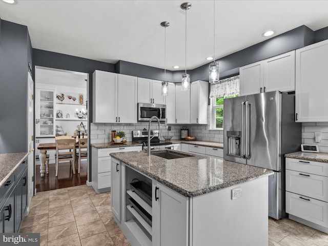 33759 Bay Ridge Ln, Lewes, DE 19958 - kitchen featuring appliances with stainless steel finishes, backsplash, a center island with sink, dark stone countertops, and white cabinetry