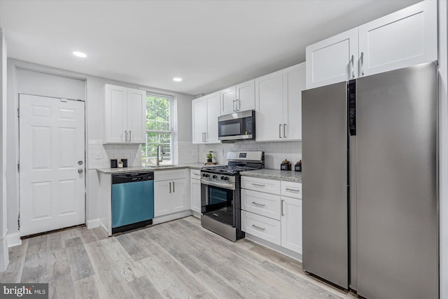 kitchen featuring appliances with stainless steel finishes, a sink, white cabinets, backsplash, and light wood-style flooring