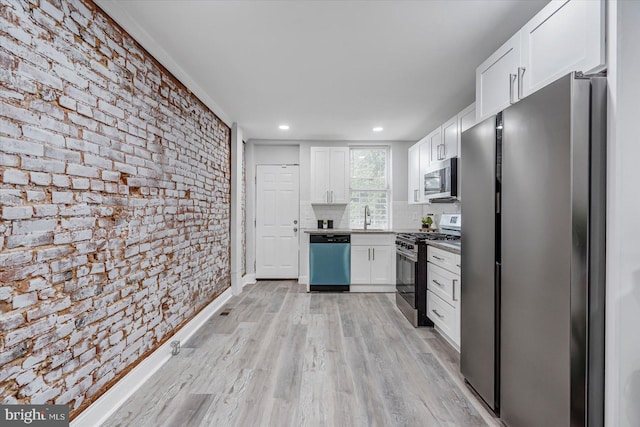 kitchen featuring appliances with stainless steel finishes, a sink, white cabinetry, brick wall, and light wood-style floors