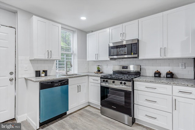 kitchen with appliances with stainless steel finishes, a sink, light wood-style floors, white cabinets, and light stone counters