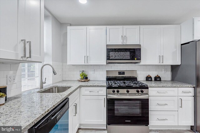 kitchen with stainless steel appliances, a sink, white cabinetry, and light stone counters