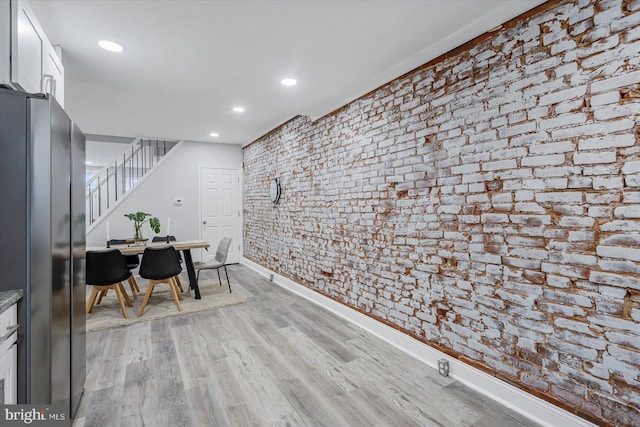 dining room with stairs, light wood-style floors, recessed lighting, baseboards, and brick wall