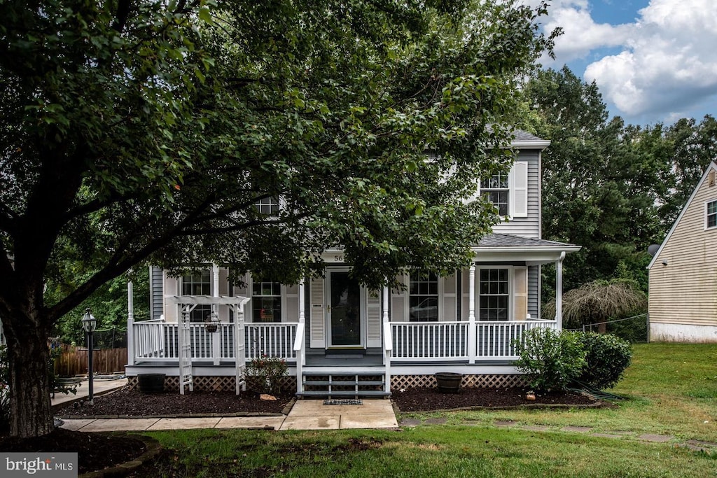 view of property hidden behind natural elements with covered porch and a front yard