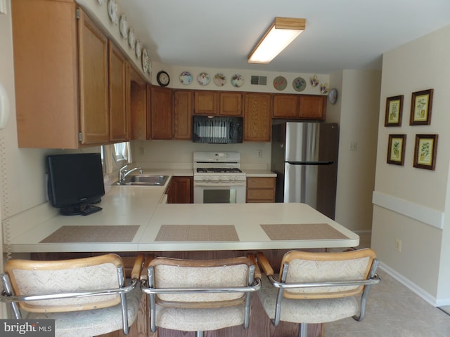 kitchen with white gas range, freestanding refrigerator, black microwave, light countertops, and a sink