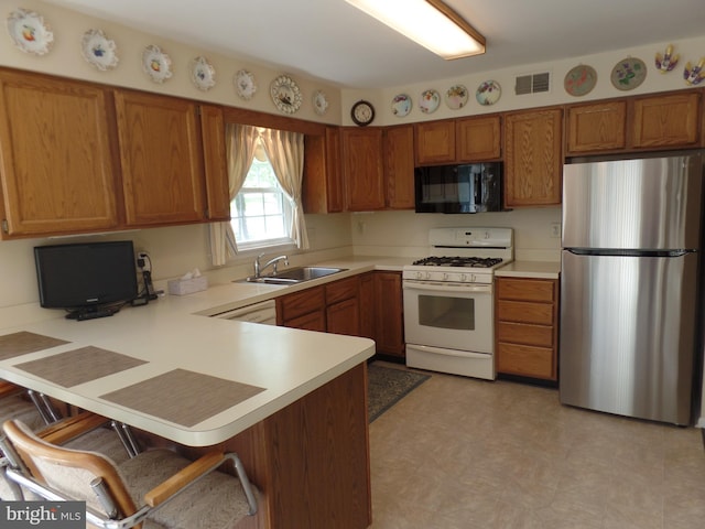 kitchen with freestanding refrigerator, black microwave, white range with gas stovetop, a sink, and brown cabinets