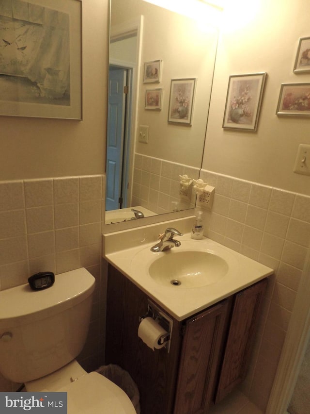 bathroom featuring tile walls, toilet, vanity, and a wainscoted wall