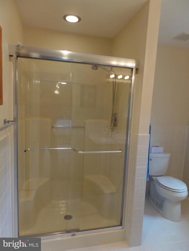 full bathroom featuring tile walls, toilet, a wainscoted wall, tile patterned floors, and a shower stall