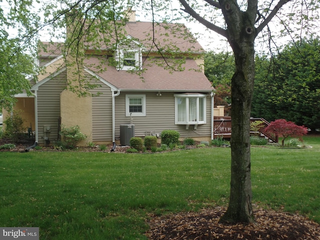 rear view of property featuring a yard, a wooden deck, a shingled roof, and central air condition unit