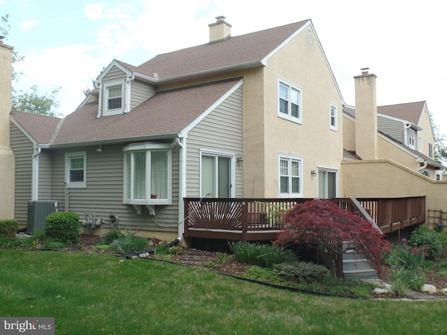 rear view of property with a deck, central AC unit, a yard, a chimney, and roof with shingles