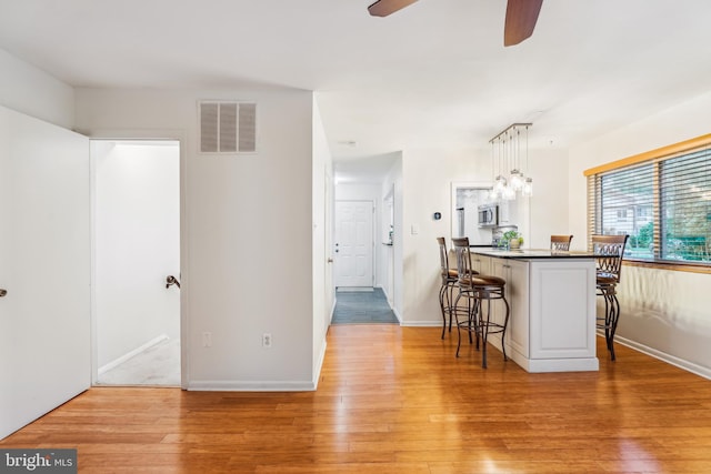 1211 Hesselius Ct, Annapolis, MD 21403 - kitchen with a kitchen bar, stainless steel microwave, light wood finished floors, a ceiling fan, and baseboards