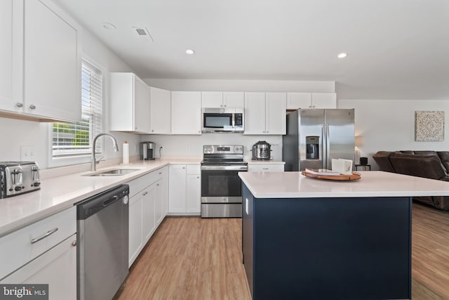 kitchen with a center island, a sink, white cabinetry, stainless steel appliances, and light wood-type flooring